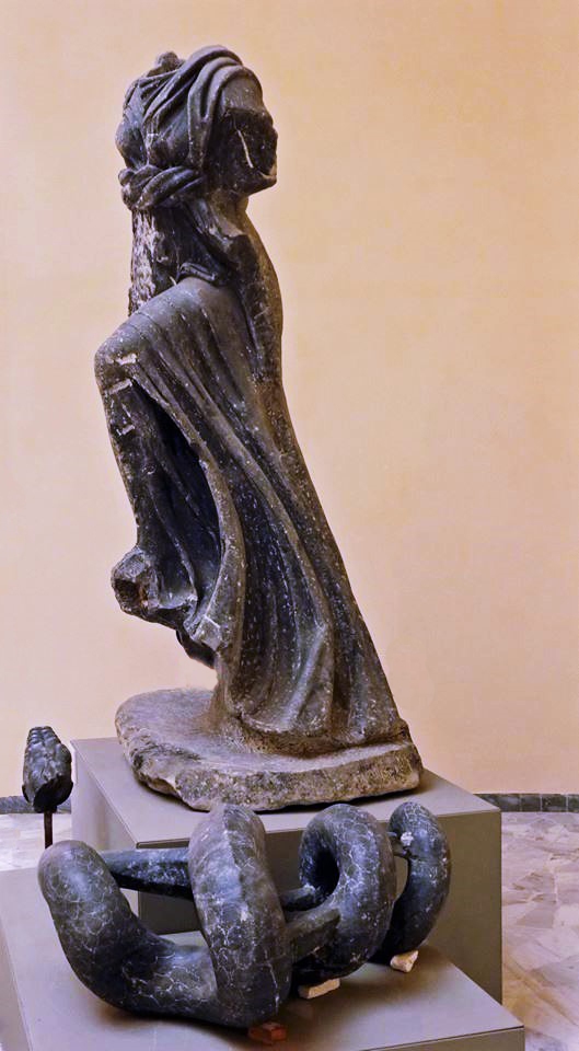 Statue of goddess Isis made of dark marble, head and arms missing, depitected in a forward movement